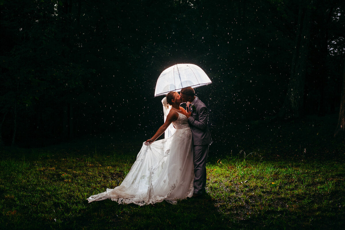 Photo of a bride and groom kissing under an umbrella as it rains