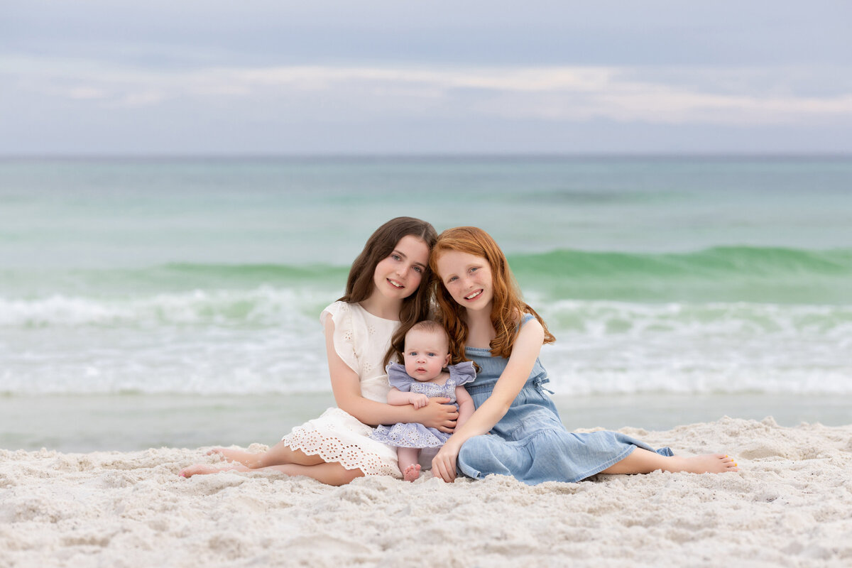 Three siblings sitting in the sand together smiling