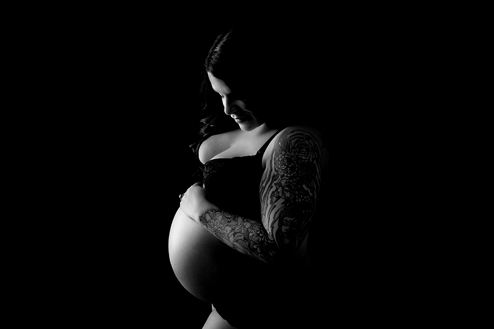 Black and white image of a woman in black underwear smiling down at her pregnant bump