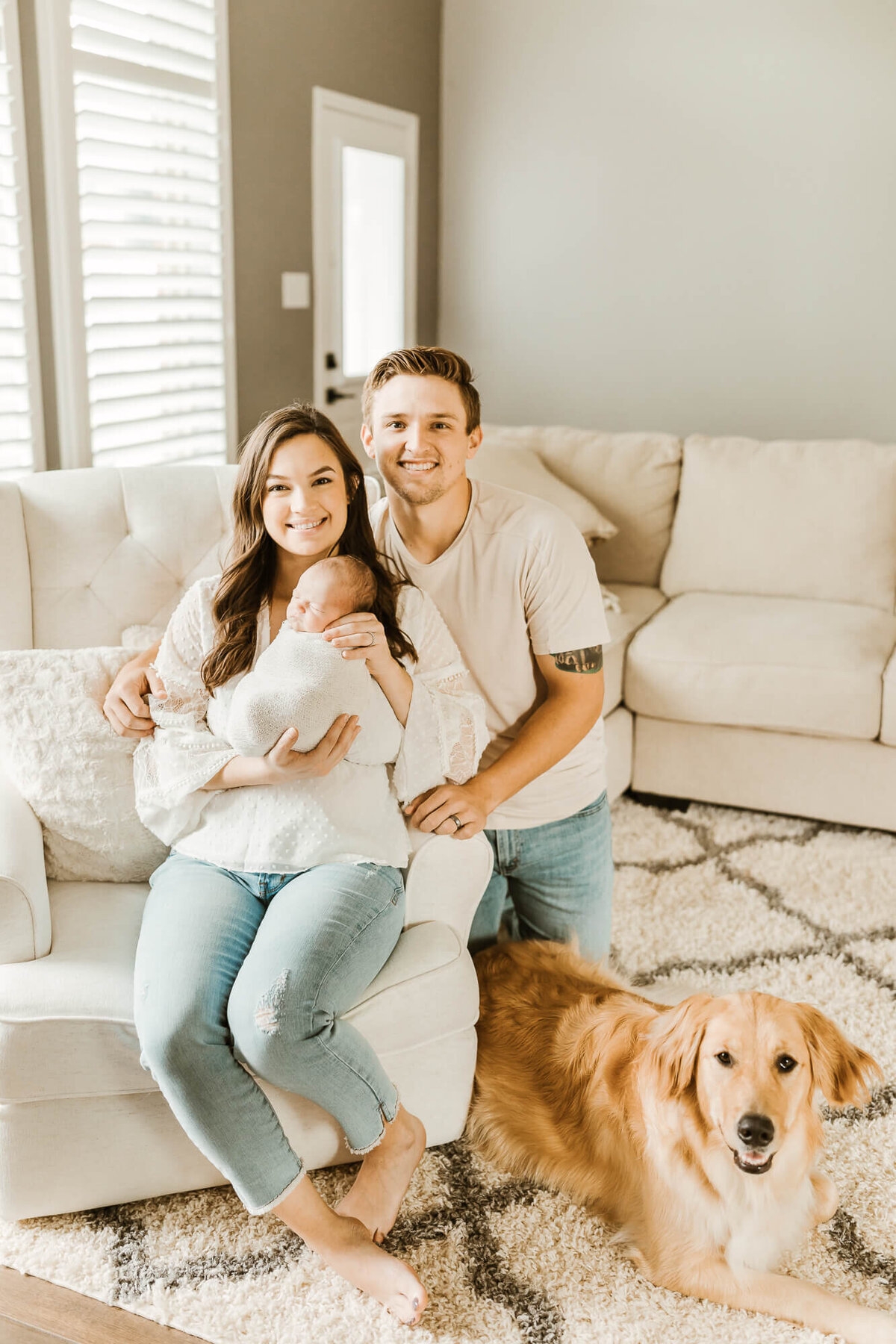 Mom and dad holding newborn infant with dog at their feet.