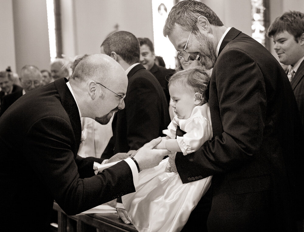 Baby flower girl in satin dress shaking hand with a groom, wearing black in the church