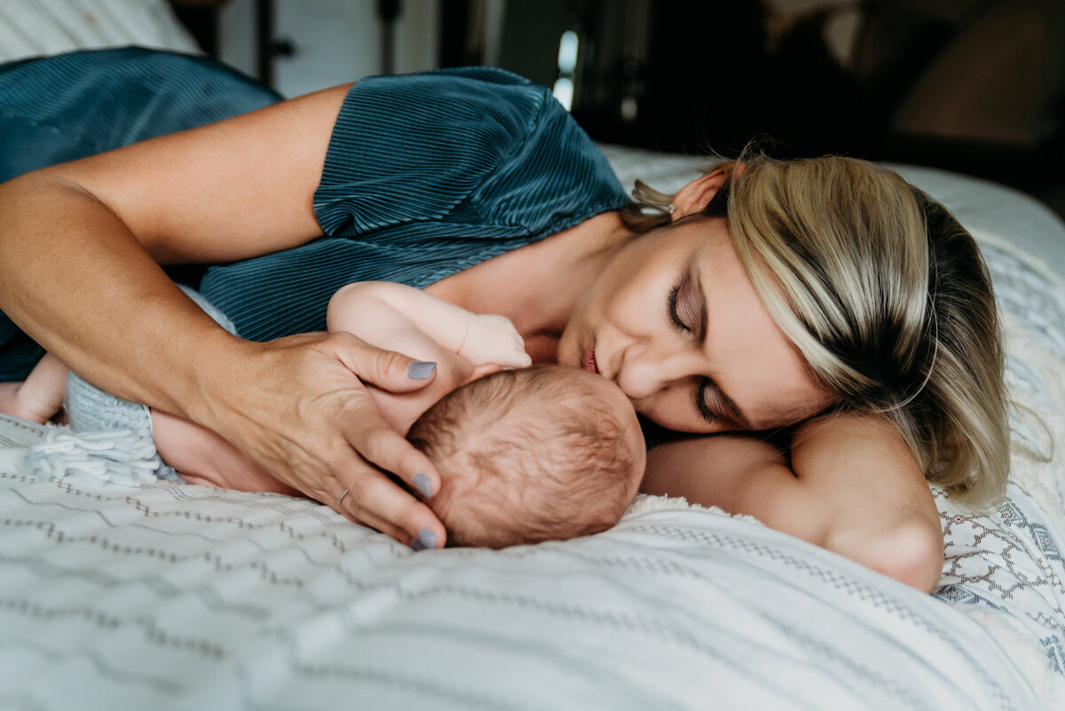 Newborn Photographer, a new mother lays on her bed with her little baby, giving him kisses