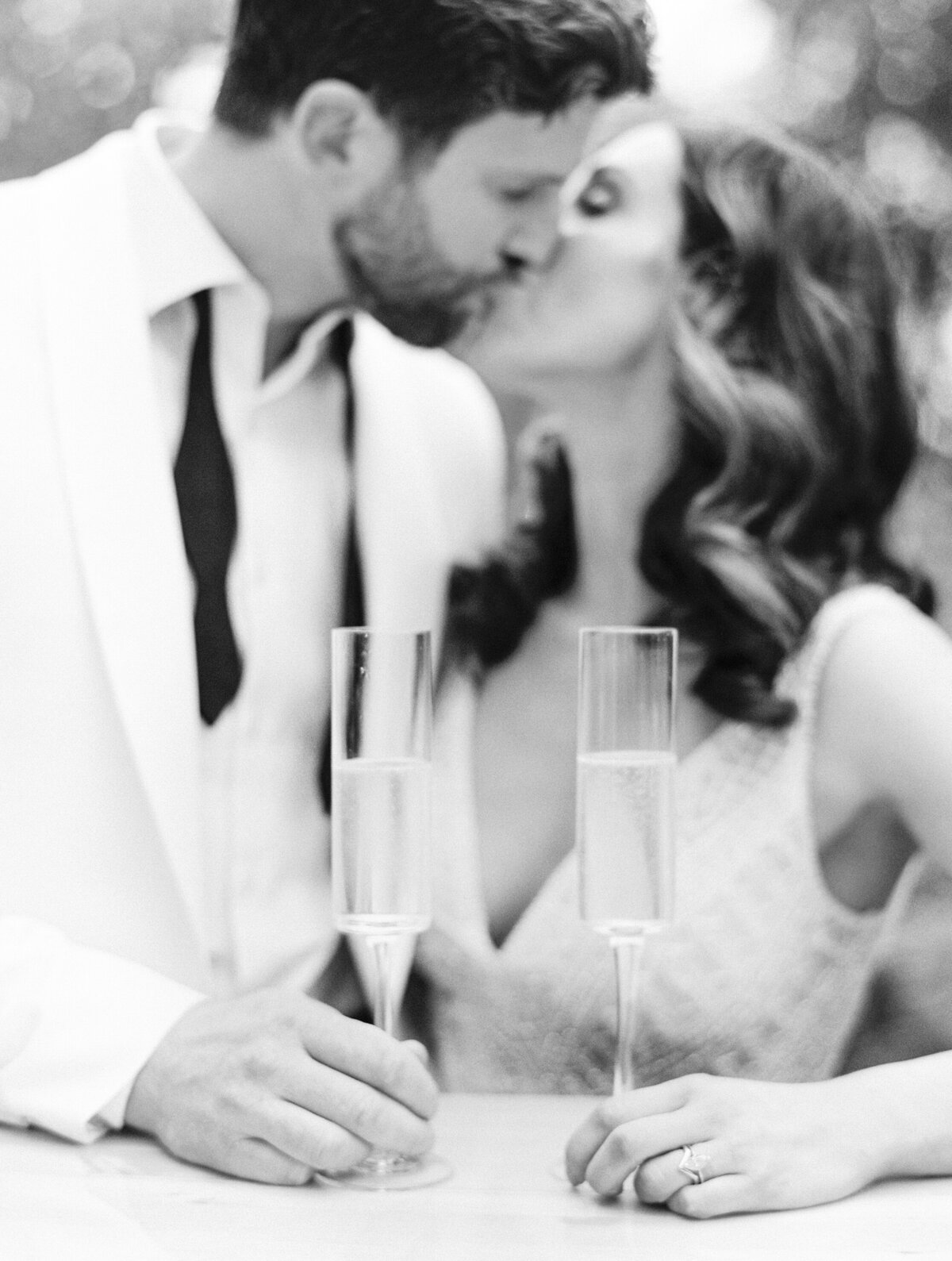 a black and white photo of a bride and groom kissing with champagne glasses in hand
