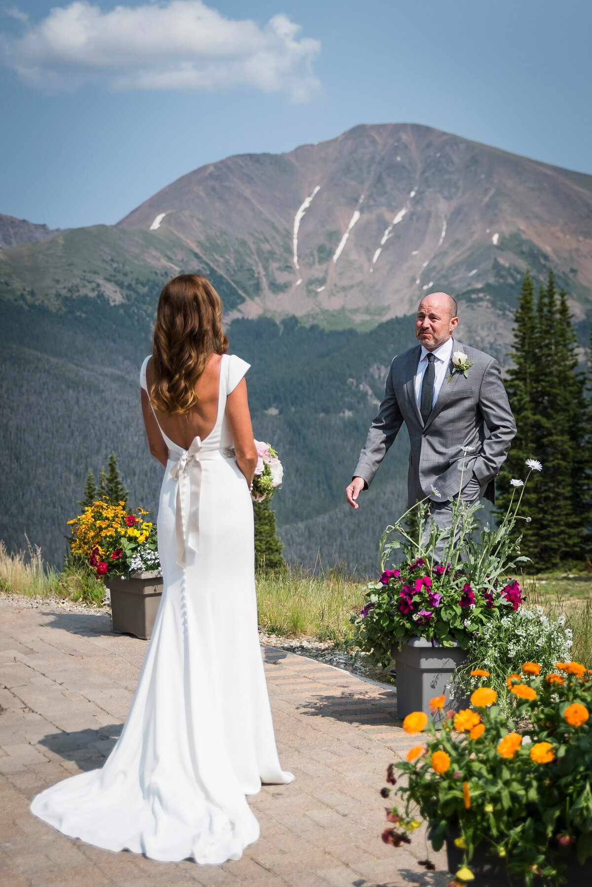 A groom reacts emotionally as he sees his bride for the first time with a mountain landscape in the background.