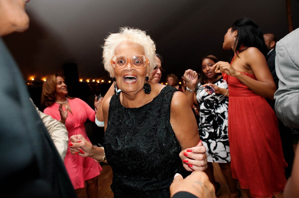 a grandma in fun orange glasses dances and laughs during the wedding reception
