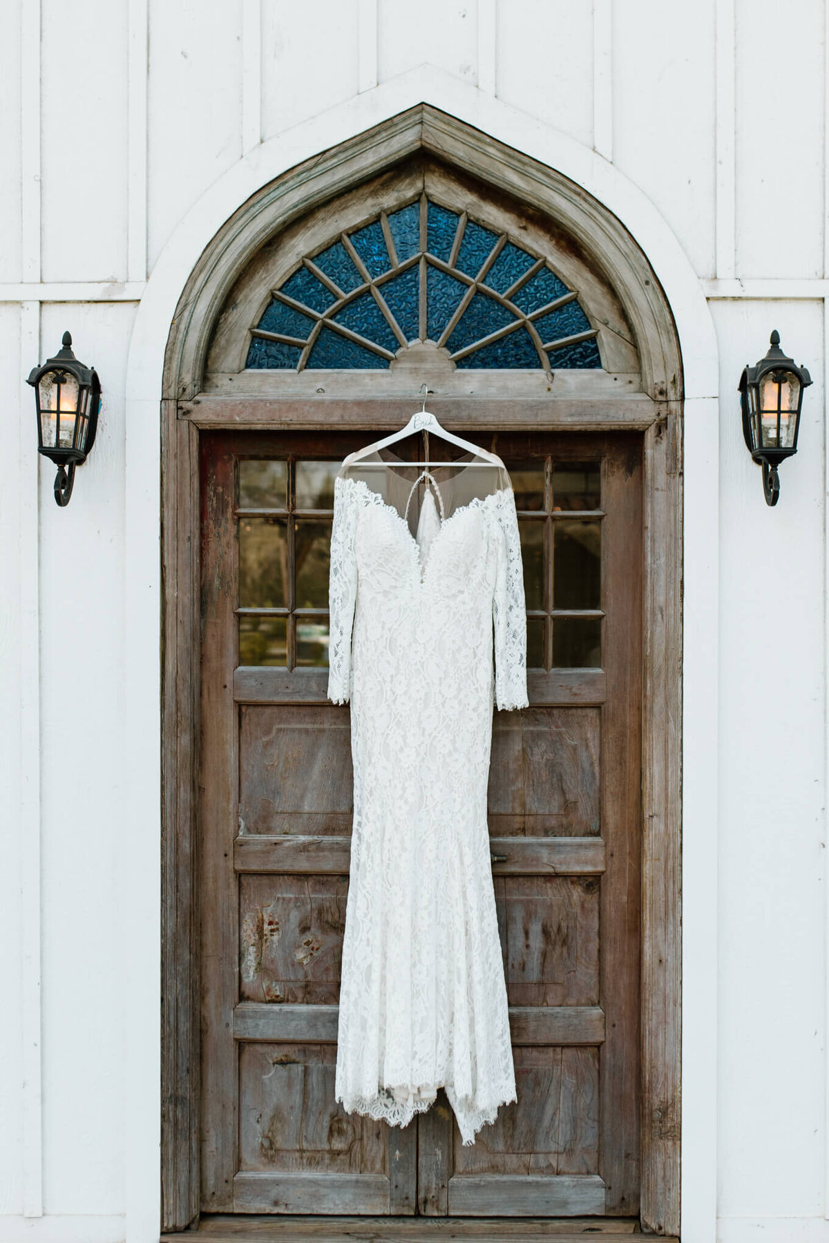 white lace wedding dress hanging on chapel doors of wedding chapel at Four Fifteen Estates Wedding and Elopement Venue