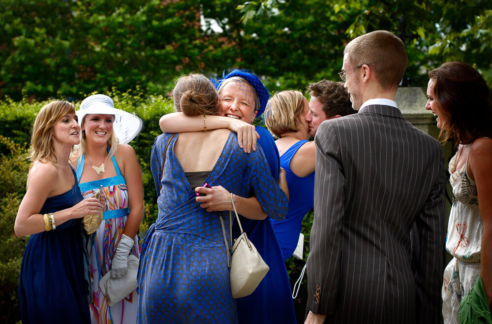 happy wedding guests in blue hugging in a church yard surrounded by friends