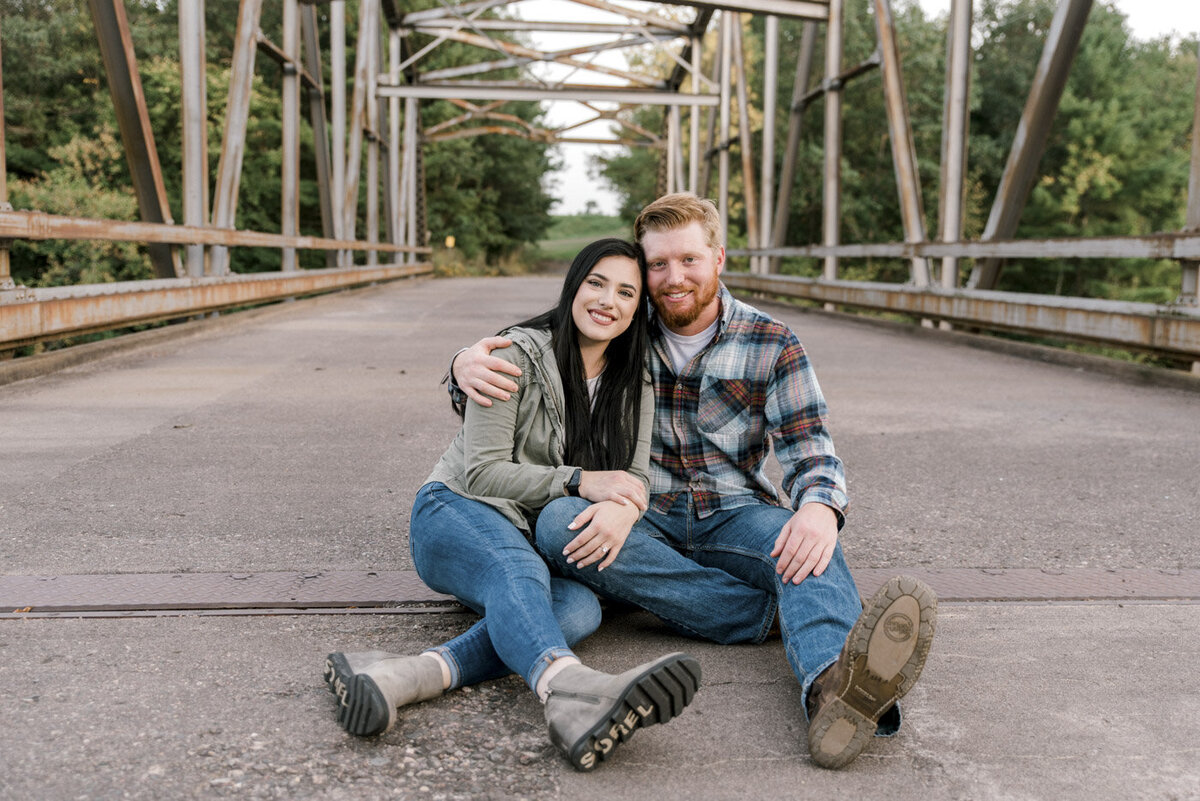 engaged couple sitting on a bridge
