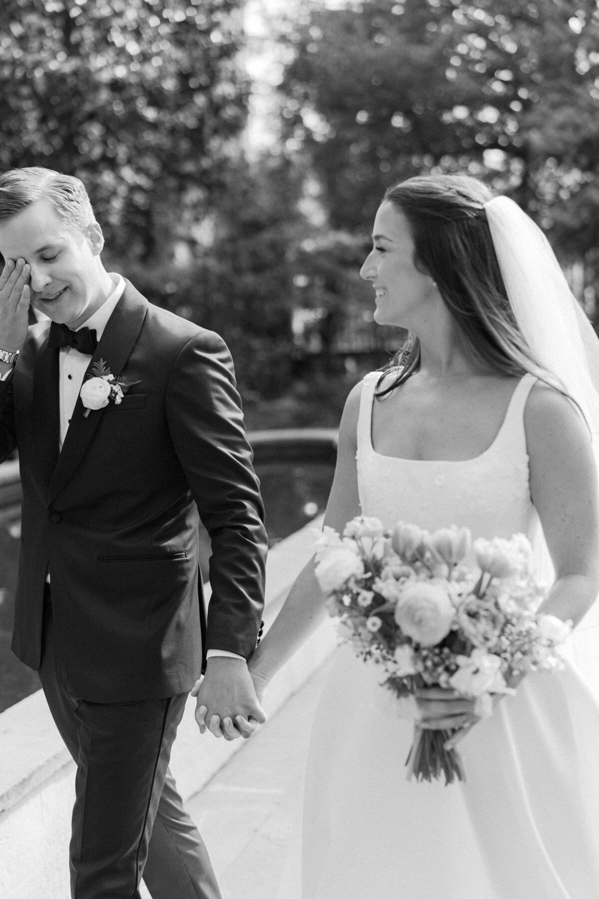 Groom wipes away tears while walking with bride to outdoor spring ceremony at William Aiken House. Intimate, emotional moments captured by wedding photographer. Black and white wedding photographer. Kailee DiMeglio Photography.