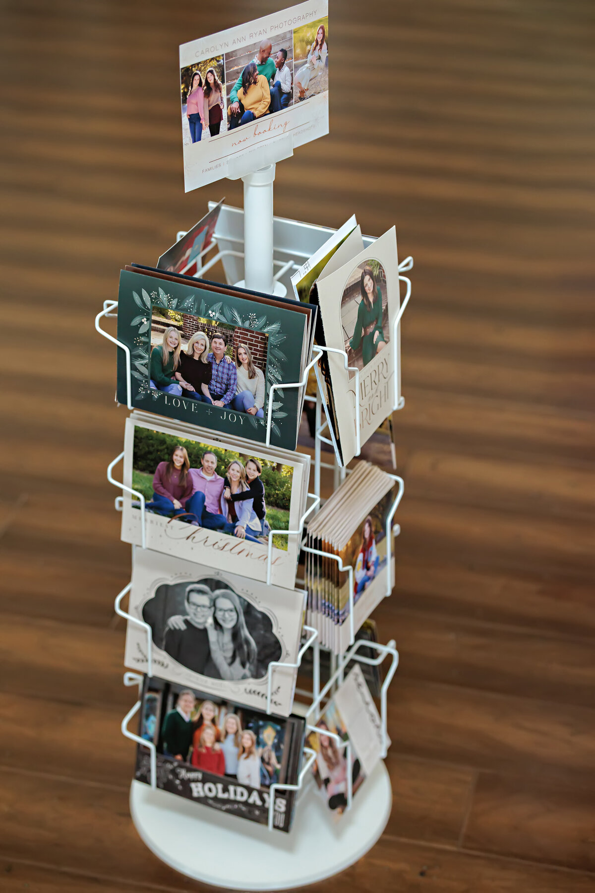 Custom press printed high school senior announcement cards and family holiday cards displayed on a tall rotating rack, showcasing a variety of designs, colors, and layouts in a professional studio setting.