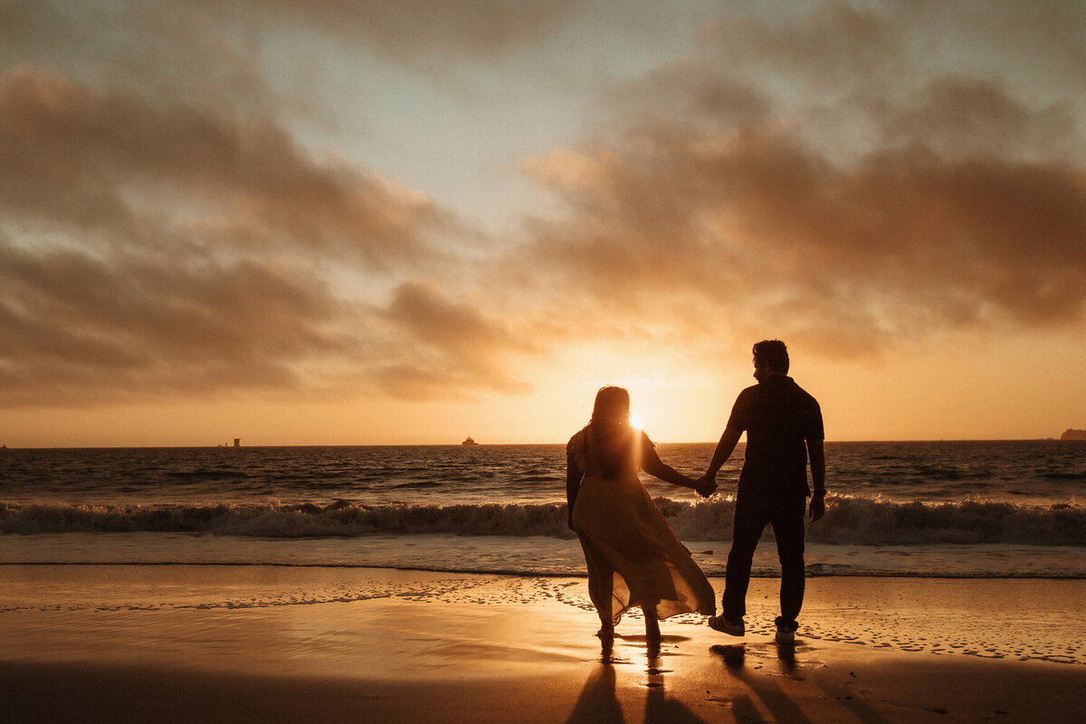 Couple holding hands engagement at golden hour sunset at San Francisco beach.
