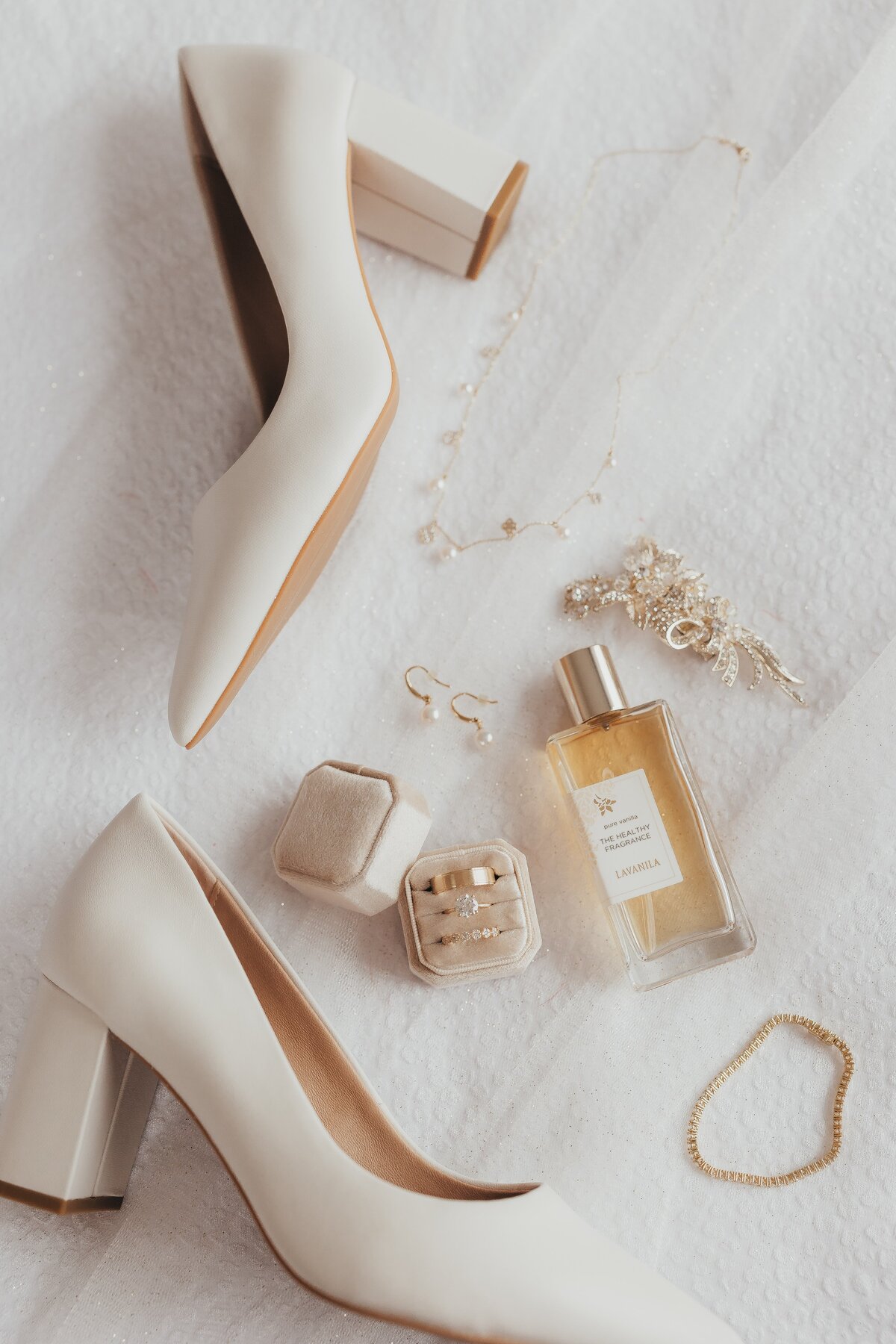 White high-heeled shoes with jewelry and a perfume bottle on a textured white fabric, perfect for Iowa weddings.