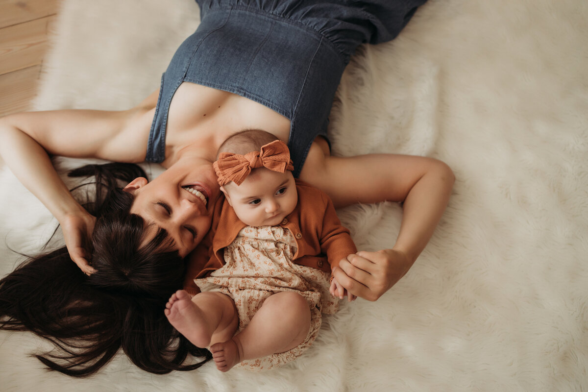 overhead photo of mom  and three month old baby girl laying on white rug