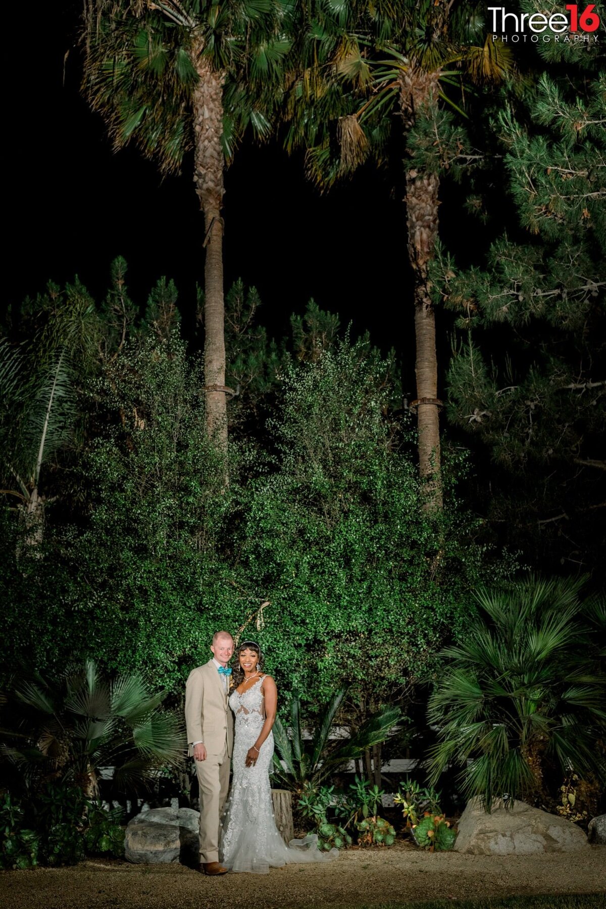 Bride and Groom pose together in front of large green foliage