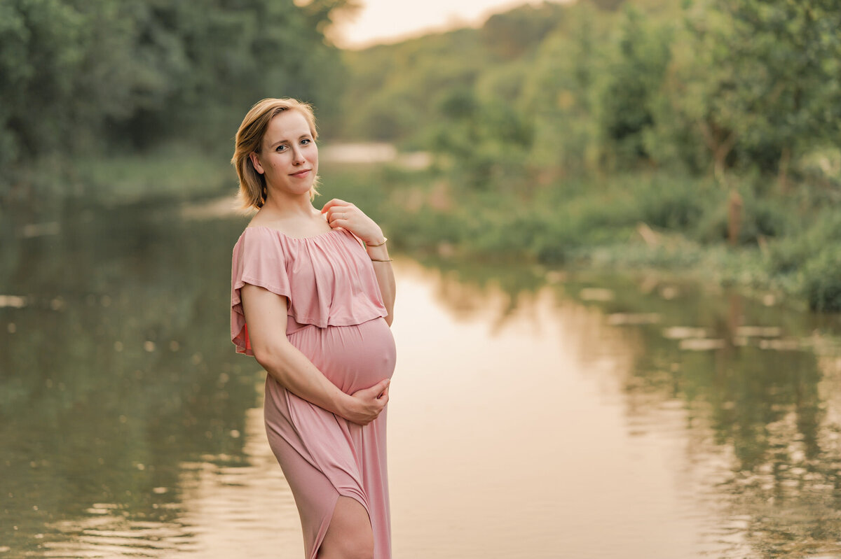 Pregnant woman stands in front of the water at Crescent Bend Nature Center during maternity photos with Cassey Golden Photography.