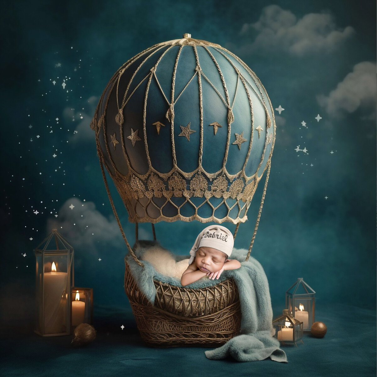 A baby peacefully sleeps in a decorative hot air balloon basket adorned with stars, while wrapped in a soft blanket, created by professional photographer, Christy Whitehead. Candles and lanterns surround the scene, set against a dreamy, cloudy backdrop.