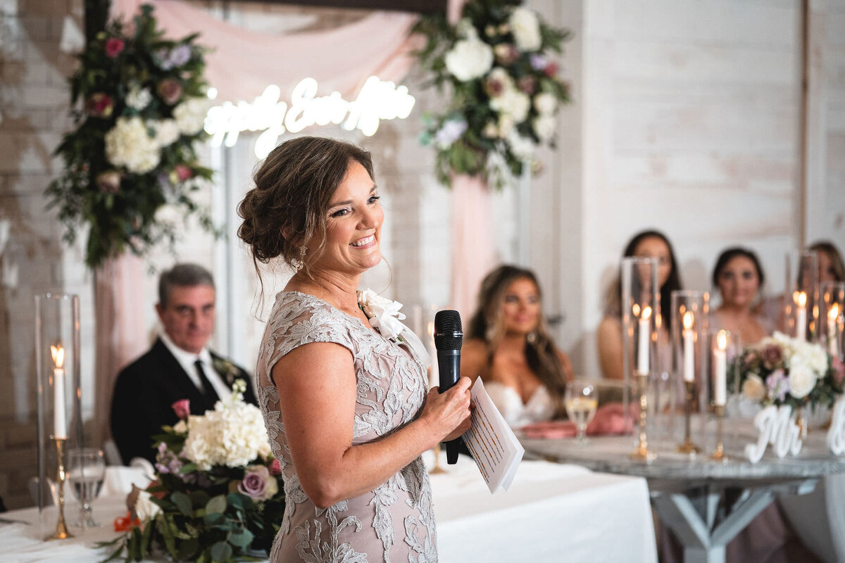 Wedding speech given by mom with wedding flowers and bridal party in the background smiling