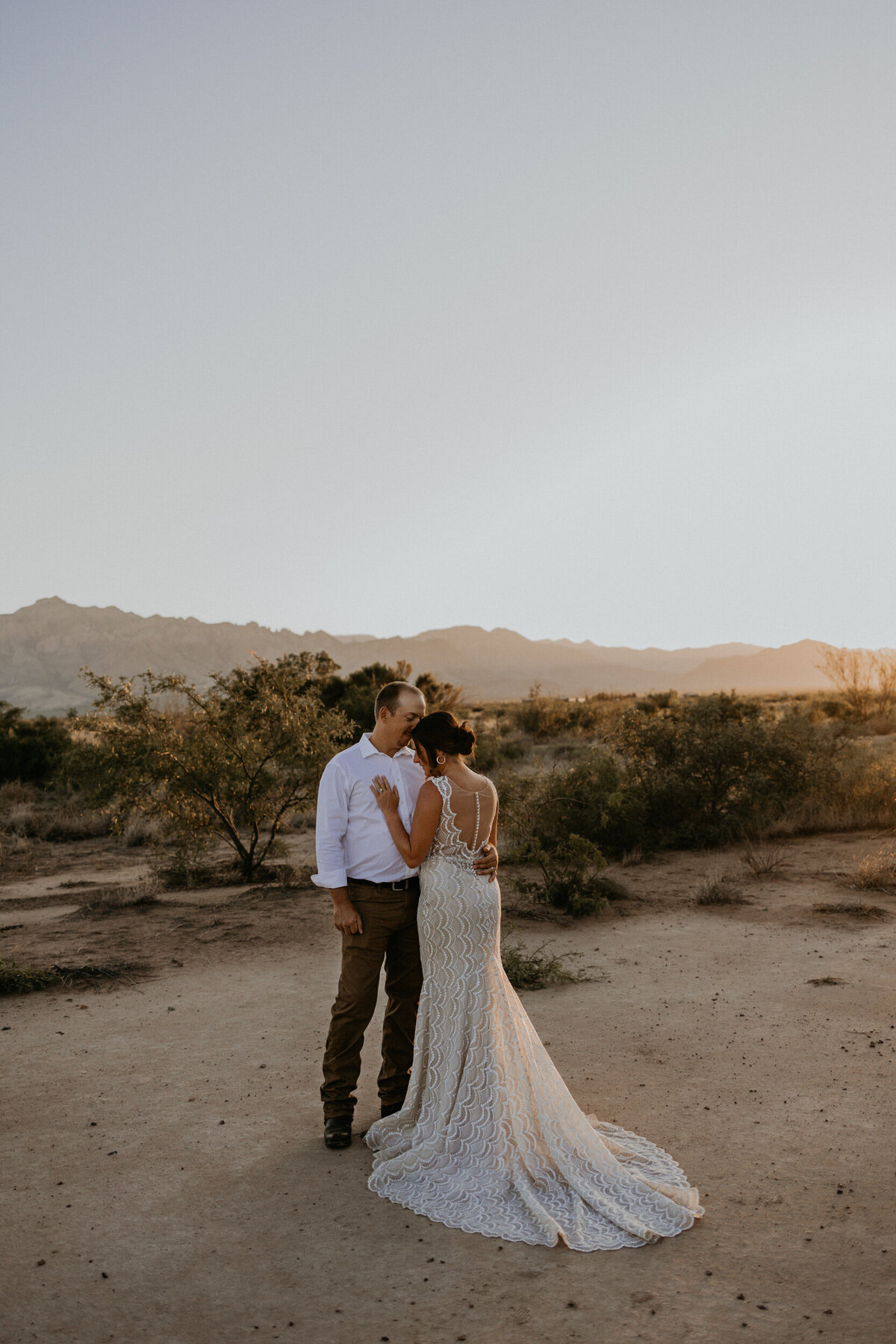 bride and groom standing together in the desert with the sun setting behind them
