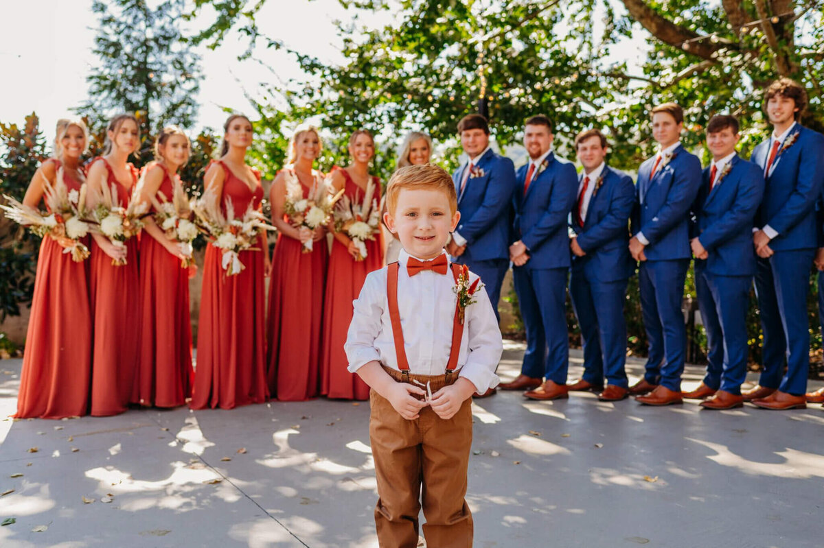 Photo of a ringbearer smiling while the wedding party is standing in the background