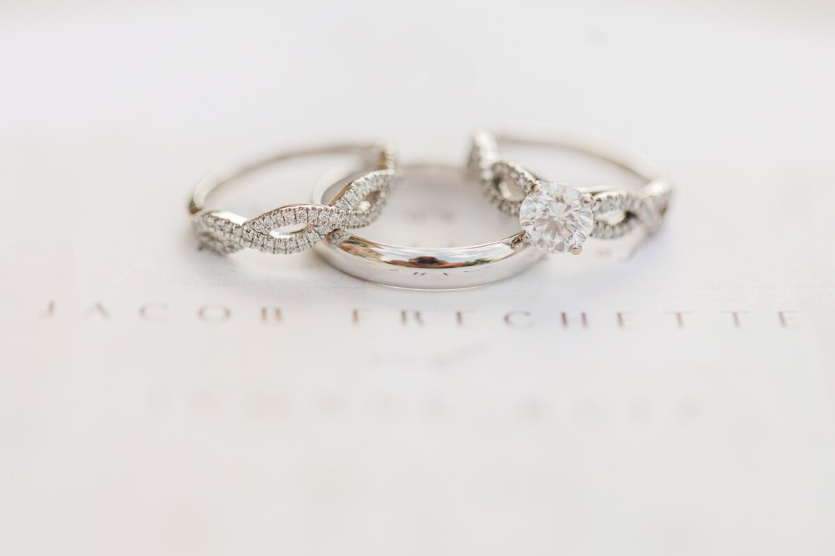 Two elegant diamond rings placed on a soft white surface with text "Iowa weddings" subtly visible in the background.