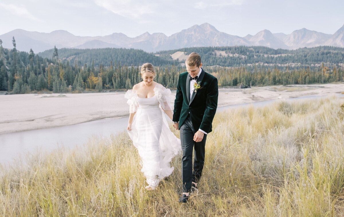 bride and groom walking in a open field in banff national park with rocky mountains in the background photographed by Alberta wedding photographers David and Breanne Heidrich