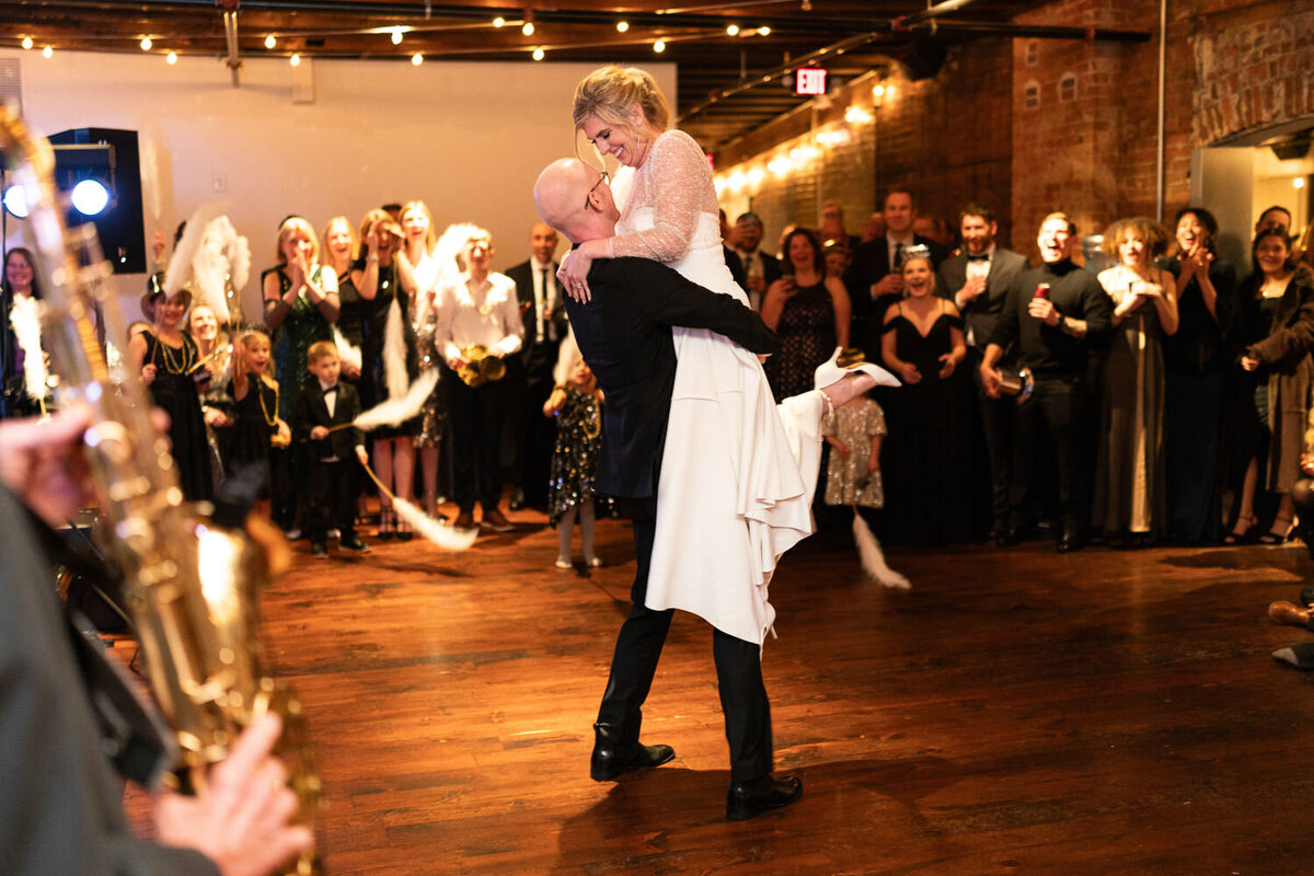 Groom lifts bride during first dance in front of the guests.