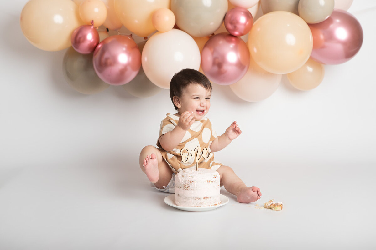 First birthday girl eating a pink cake with a pink beige and white balloon garland