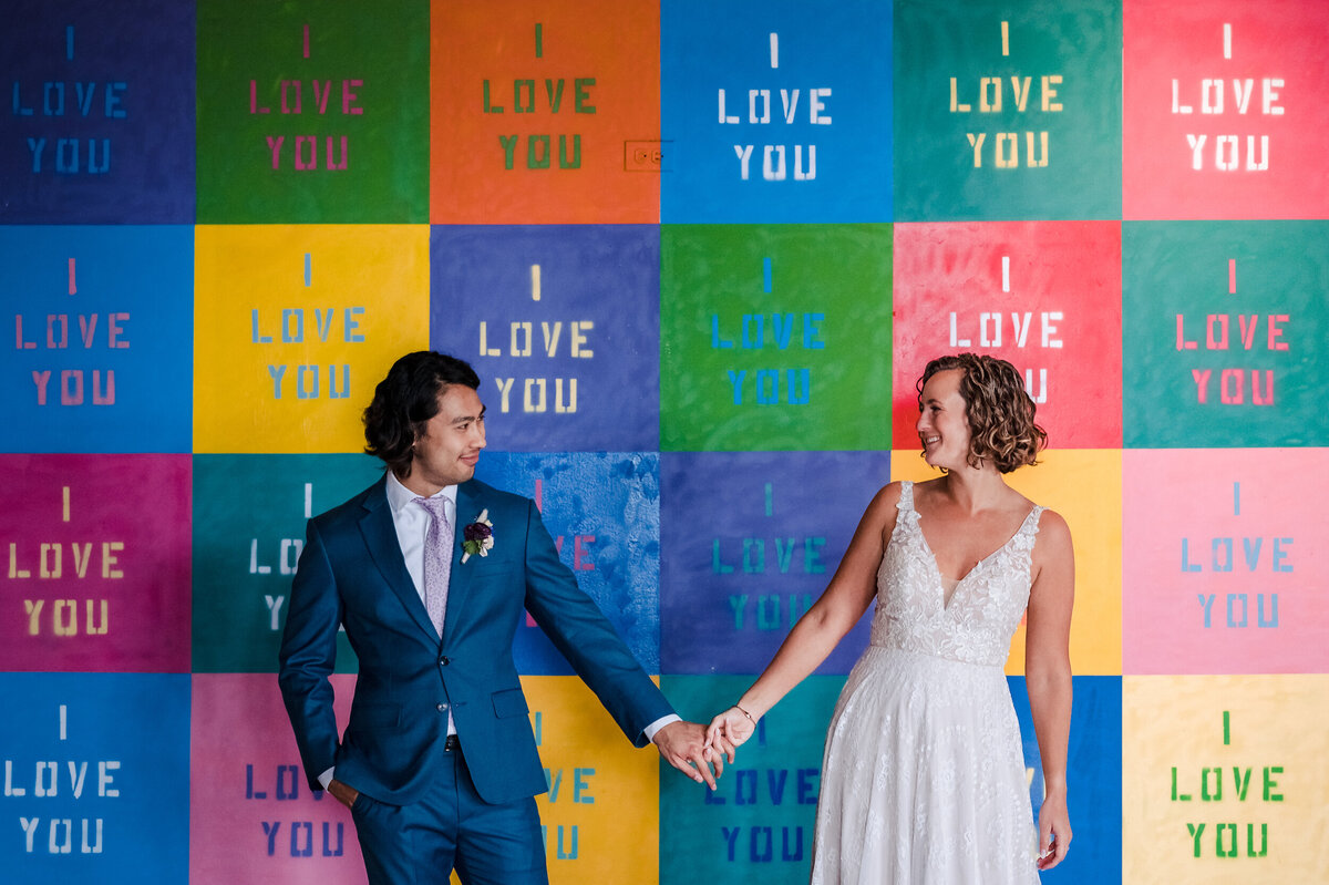 A bride and groom hold hands in front of the I love you mural before getting married at Lacuna Lofts in Chicago, IL