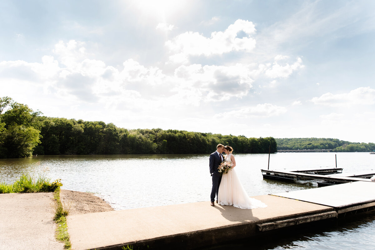 bride and groom stand on dock by water at morraine state park