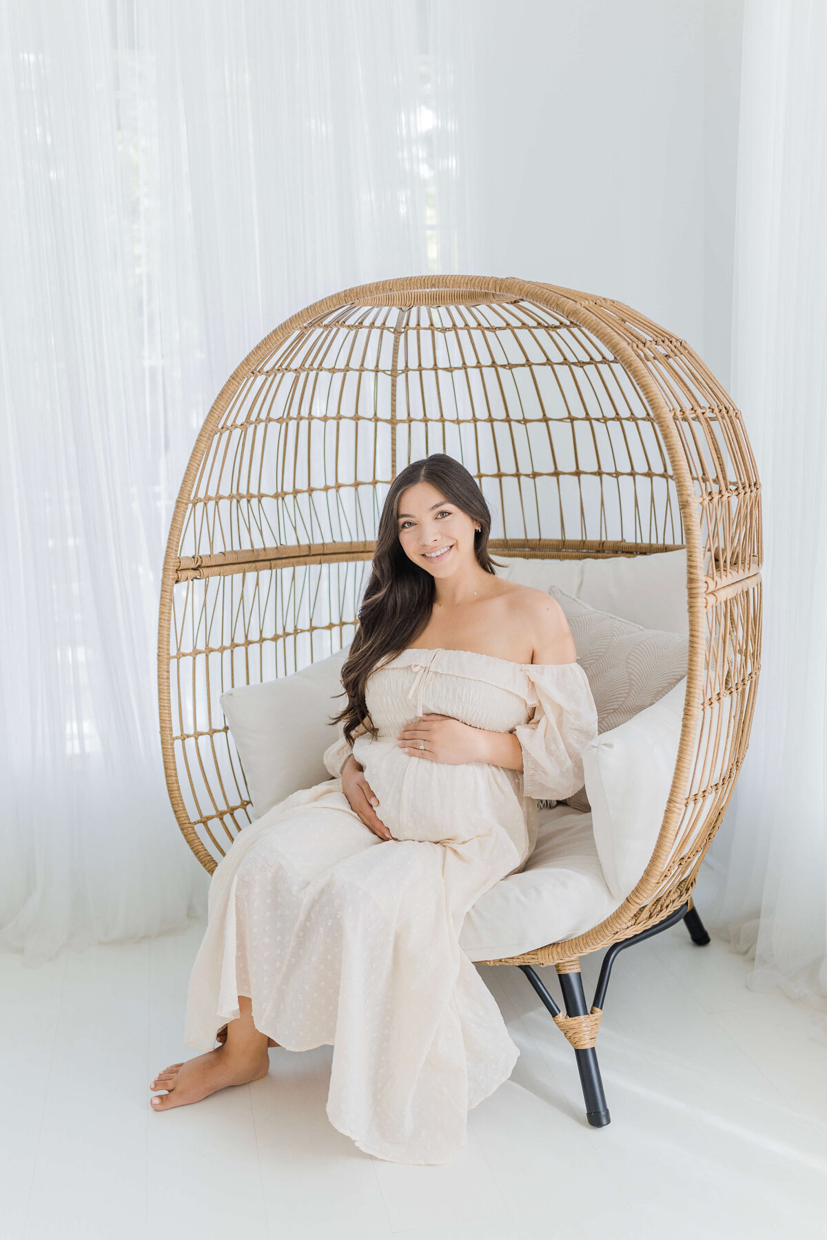 Mother sitting in egg chair during studio maternity photos in Folsom, CA