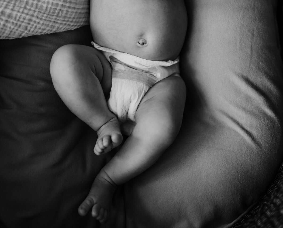 Newborn Photographer, baby belly and legs are snuggled beside dad