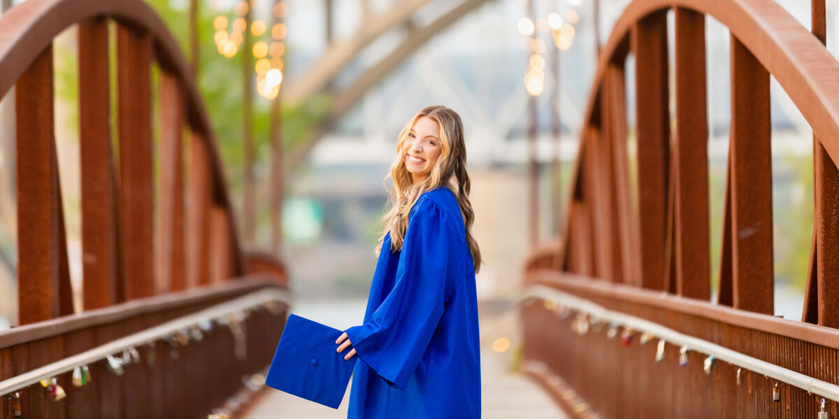 A girl in a blue cap and gown on a bridge downtown