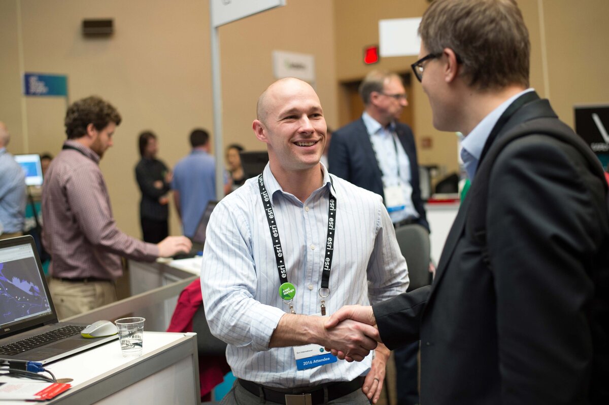 Esri user shakes hand with attendee at user conference. the largest GIS conference in the world