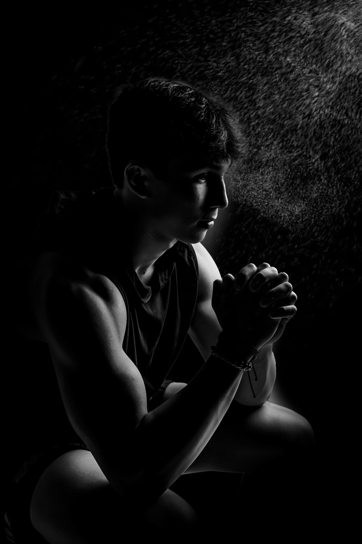 An athletic boy from Kettle Moraine High School sits in our studio with clasped hands having a black and white portrait taken.