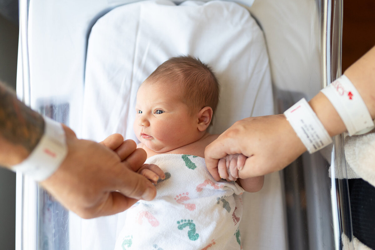 Newborn girl holding mom and dad's hands in the hospital for her fresh 48 session.