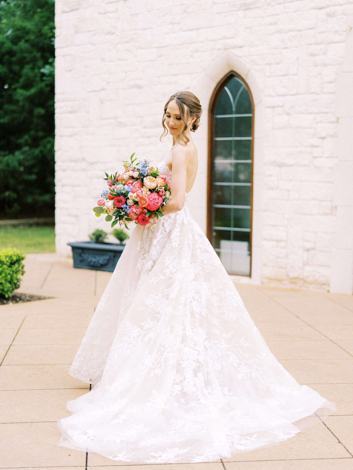 Timeless bride stands outside wedding chapel in Monique Lhuillier wedding dress with colorful bridal bouquet
