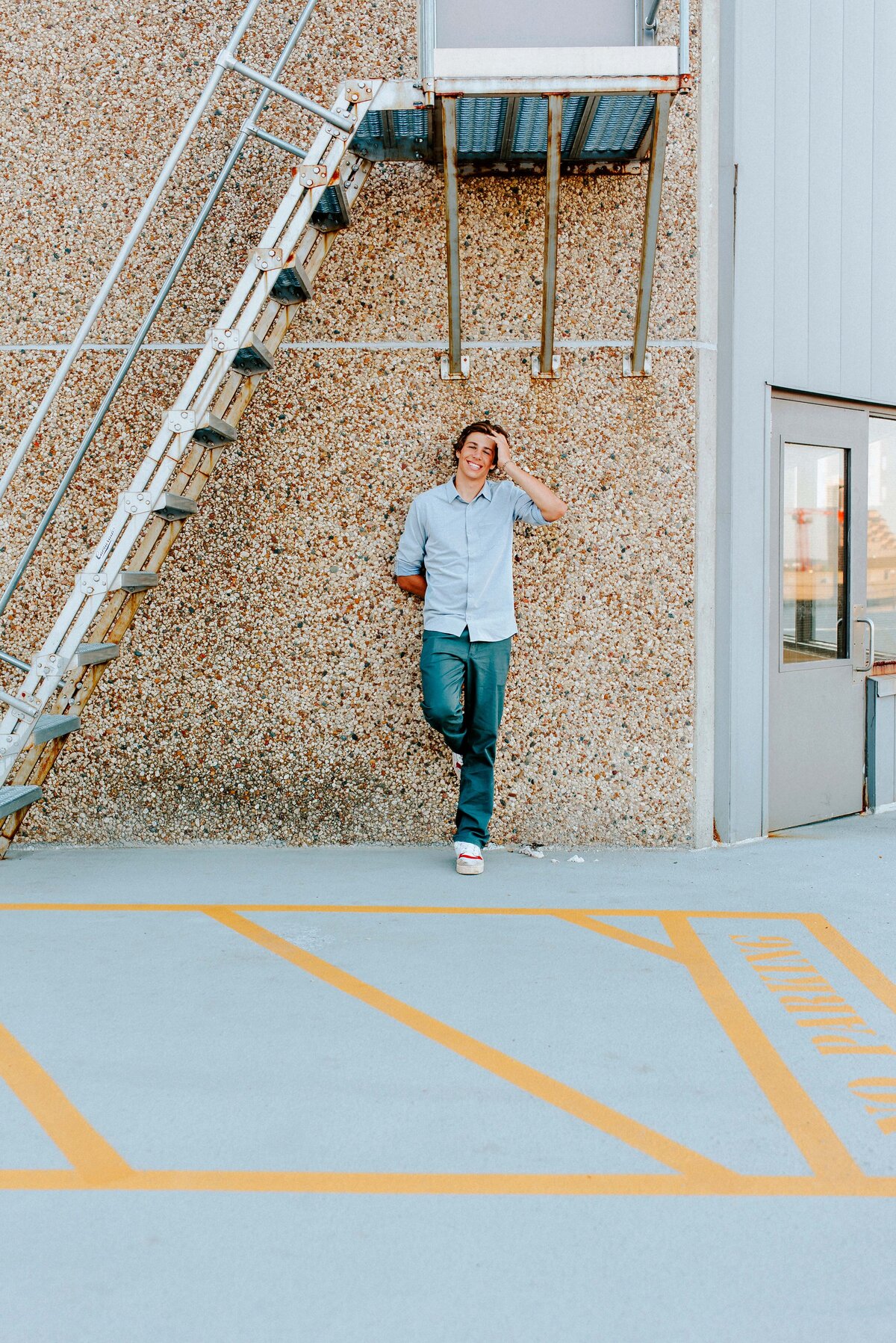 An Edina High School senior graduate stands confidently on the rooftop of a downtown Minneapolis parking garage, leaning against a wall near a flight of stairs. This dynamic senior portrait captures the spirit of achievement and adventure as he takes his place on the city skyline, marking the culmination of his high school journey.
