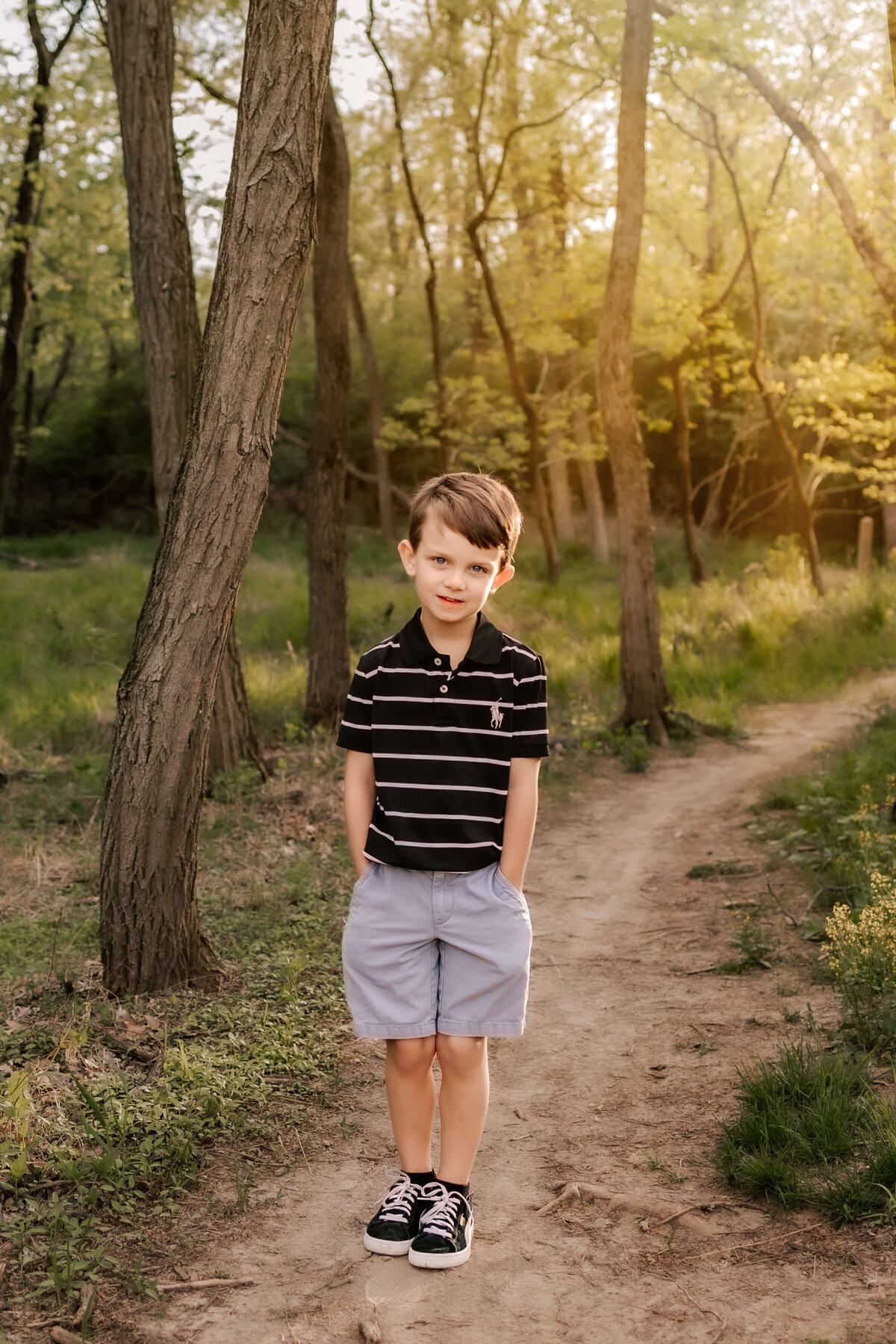 A little boy standing on a dirt pathway in the middle of the forrest.