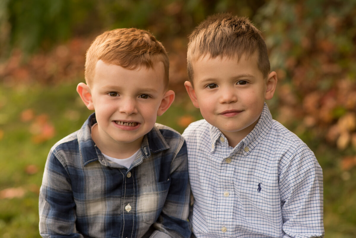 Two young brothers smiling at camera with fall leaves
