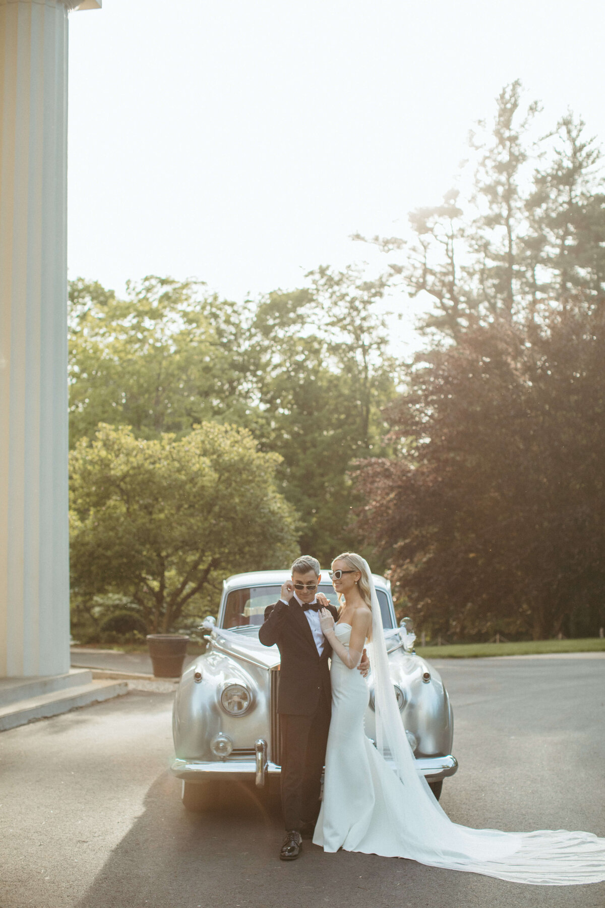 Bride and groom wearing sunglasses in front of vintage car