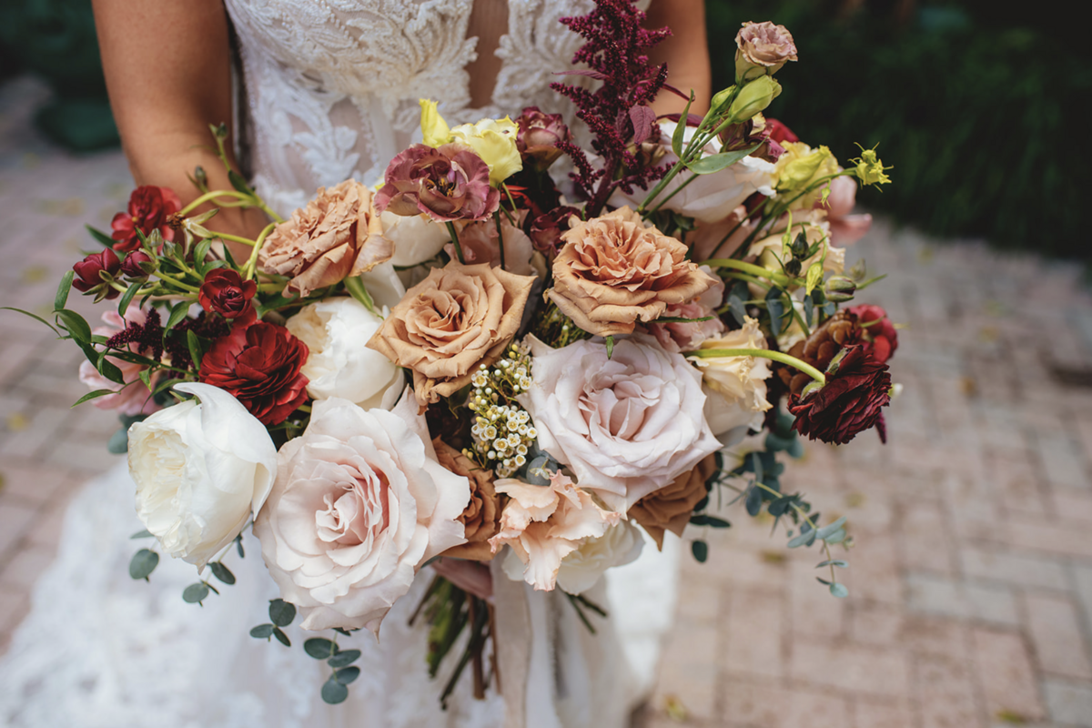 Bride holds red, white, pale pink and orange roses in a large bouquet outside of Fort Lauderdale venue, Holly Blue.
