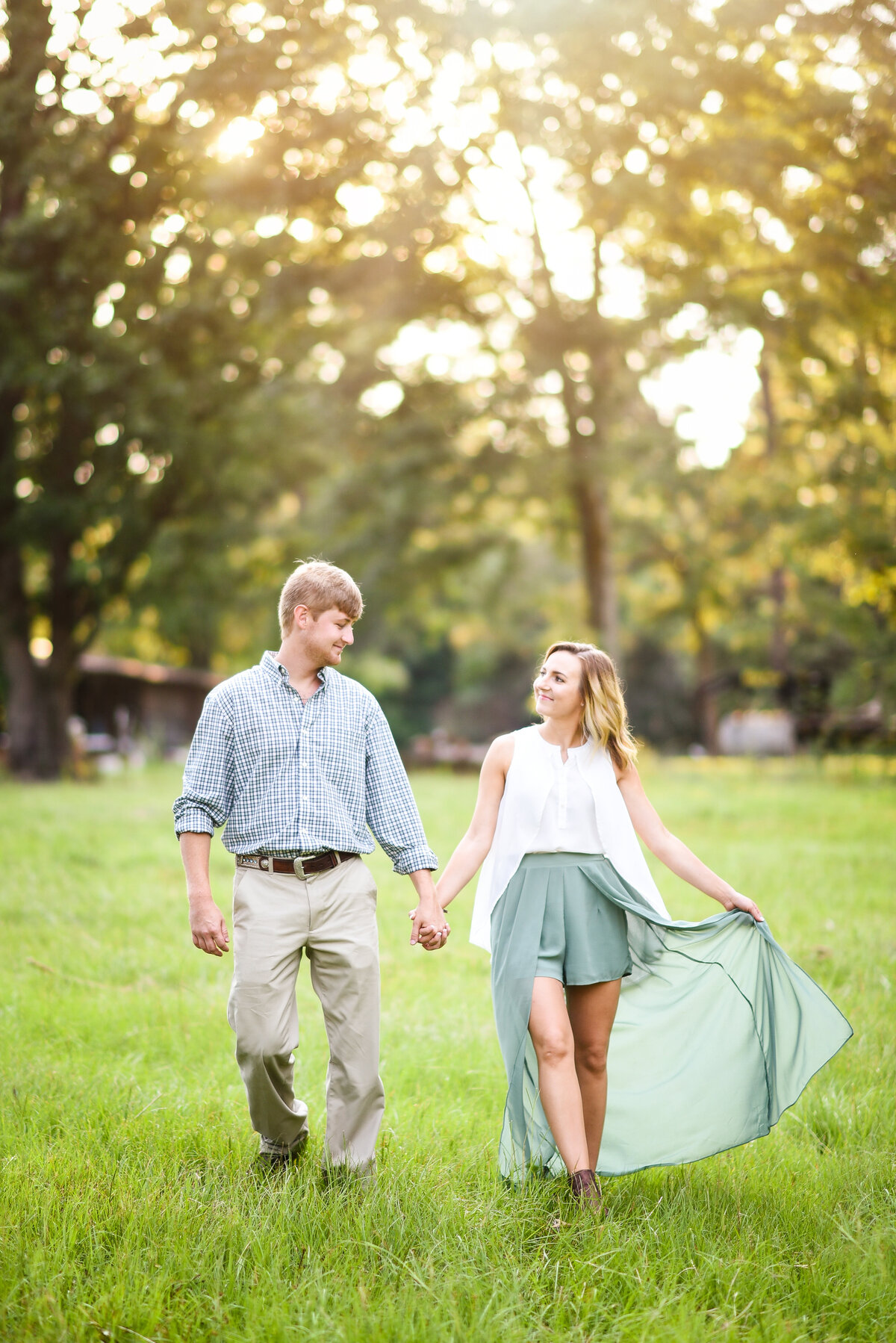 Beautiful Mississippi Engagement Photography: couple walks holding hands in a field during sunset with bride in flowy skirt