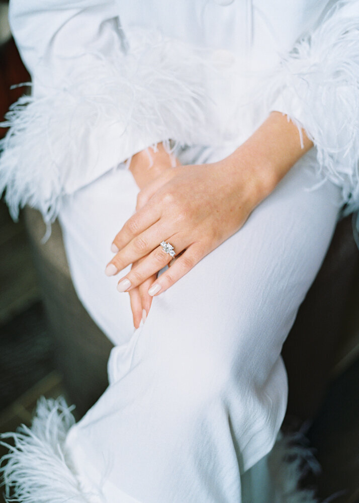 bride wearing white feather trim silk pyjama and showcasing luxury engagement ring