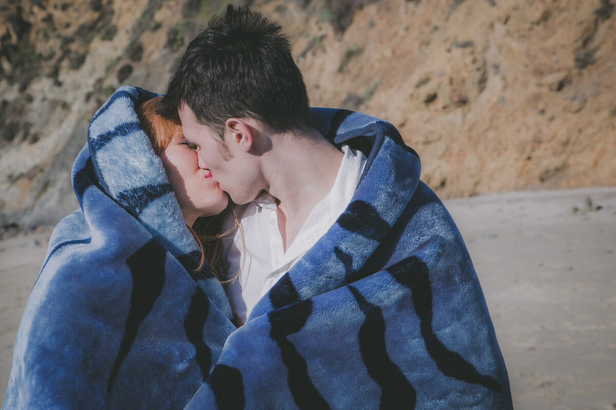 Couple keeps warm and kisses at Pfeiffer beach.