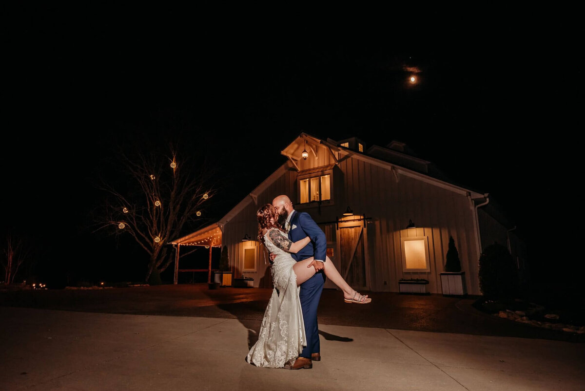 photo of a Bride and groom doing a dip in front of an illuminated barn at night