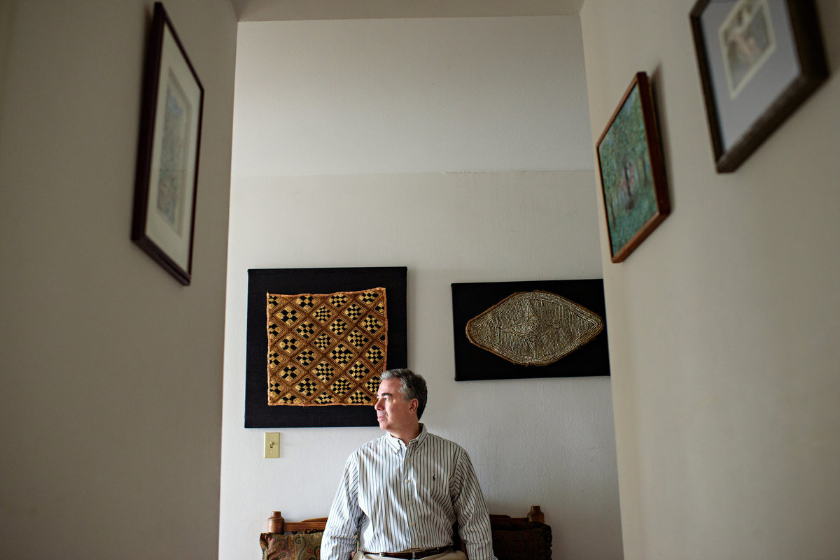 A man sits on a bench in the hallway of his home for this environmental head shot.