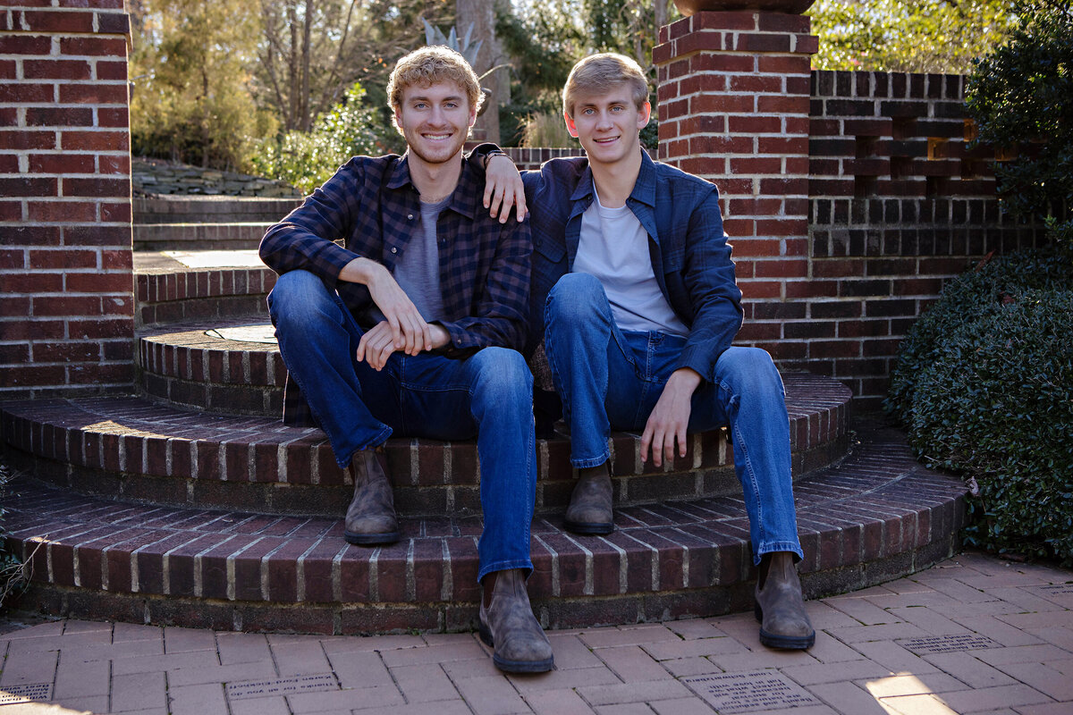 Distinguished autumn portrait of two red‑haired brothers seated on brick terrace steps framed by golden leaves at UNCC Botanical Garden Charlotte NC