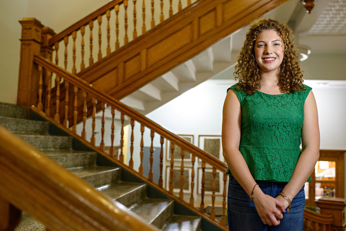 A young professional woman stands in stairs and smiles.