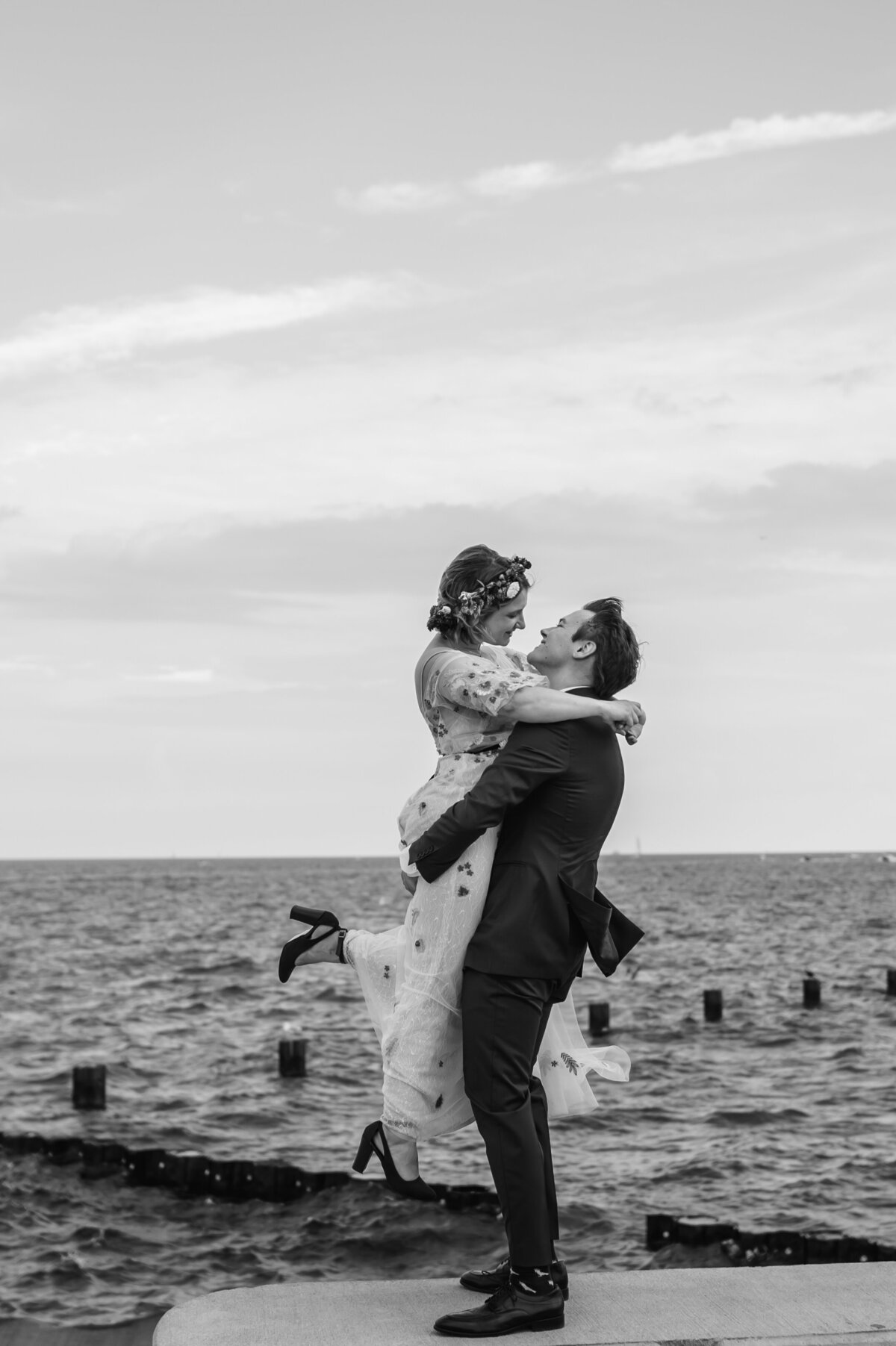 A groom picks ups his bride in front of Lake Michigan