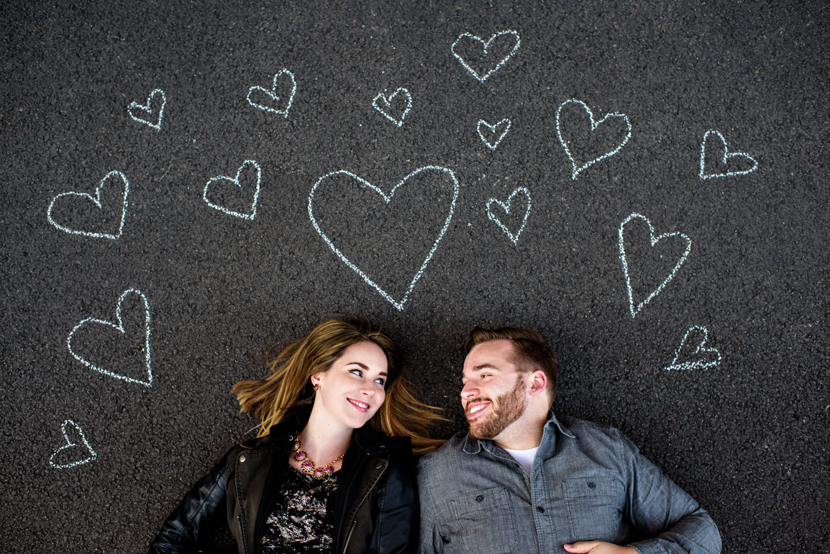 A loving couple lay on the ground surrounded by chalk hearts drawn around them.